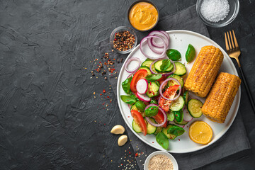 Vegetarian lunch with vegetable salad and corn in a flat white plate on a dark background.