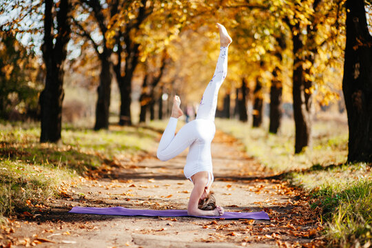 Young woman doing yoga in autumn city park near yellow birch trees