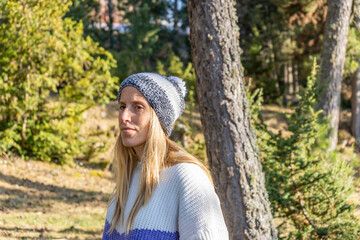 Portrait of young beautiful woman in stylish snow hat and sweater at sunset.Closeup view fashion female in woodland park landscape.