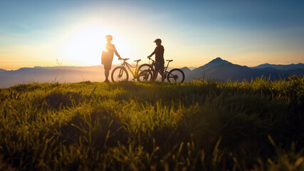 Two females on mountain bikes talking and looking at beautiful sunset