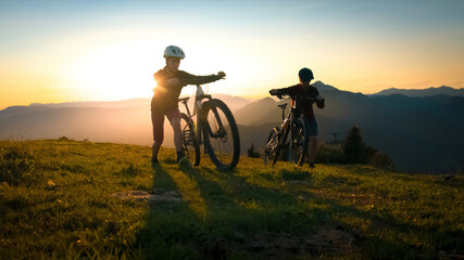 Fototapeta na wymiar Mother and daughter walking uphill with mountain bike at a sunset.
