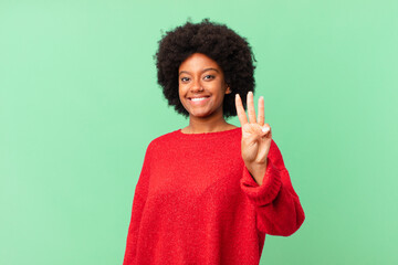 afro black woman smiling and looking friendly, showing number three or third with hand forward,...