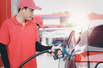 Gas station attendant in red uniform holding a fuel petrol pump nozzle against for filling up the...