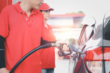 Gas station attendant in red uniform holding a fuel petrol pump nozzle against for filling up the...