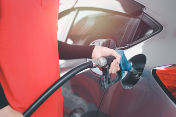 Hand of gas station attendant holding a fuel petrol pump nozzle against for filling up the car with...