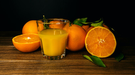 A glass of orange juice and slices of orange on a wooden board on a black background