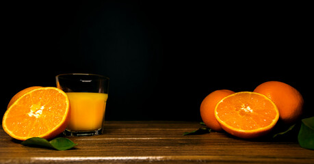 A glass of orange juice and slices of orange on a black background. Copy space in the center