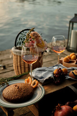 A romantic al fresco dinner overlooking the water. Close-up of two glasses of champagne, pastries and fruits in the light of the setting sun.