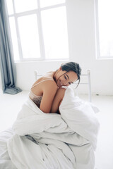 Attractive woman sits in bed wrapped in blanket.