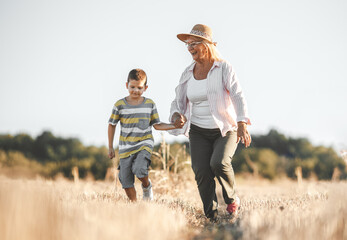 Grandmother walking on the meadow with her grandson. Relaxing and joying in sunset.		