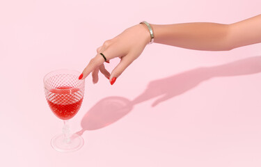 Womans hand touch glass on pink background. Manicure design trends