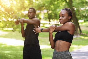 Motivated African Couple Warming Up Before Running In Park, Training Outdoors Together