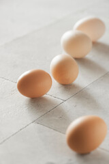 Raw chicken eggs background on white textured table with sunny light. Close up view, selective focus, copy space. Organic, healthy eating, keto diet concept.