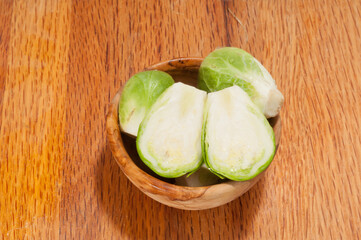 top view, close distance of a rare wood bowl , filled with halved, local, freshly picked brussels sprouts, on a wood cutting board