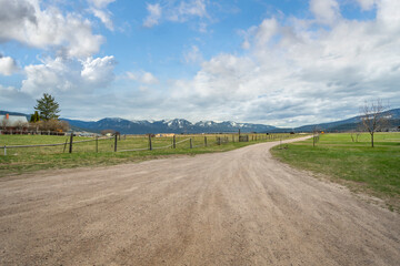 Fototapeta na wymiar A snow covered mountain range is seen from a rural country ranch and dirt road in the small town of Arlee, Montana, USA