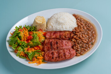 Plate with sausage, beans, rice, salad and farofa on isolated neutral background. Traditional Brazilian cuisine lunch.