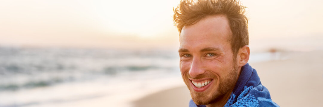 Smiling Handsome Young Man Beauty Portrait On Beach At Sunset Looking At Camera Laughing, Healthy Grin -Panorama Banner Face Of Happy Model In Towel.