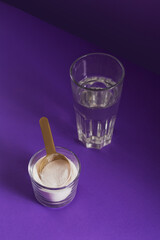 Glass with collagen dissolved in water and collagen protein powder on purple table