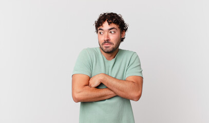 hispanic handsome man shrugging, feeling confused and uncertain, doubting with arms crossed and...