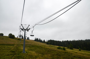 Summer cloudy landscape with empty ski lift on the green grassy hill in the Carpathian mountains,...
