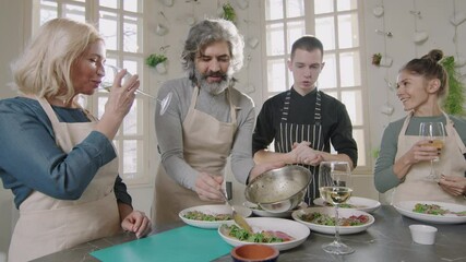 Slow-motion medium shot of small group of enthusiastic people and professional male chef talking while serving dishes during cooking class