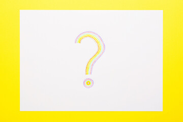 One colorful question sign on white paper on bright yellow table background. Closeup. Top down view.