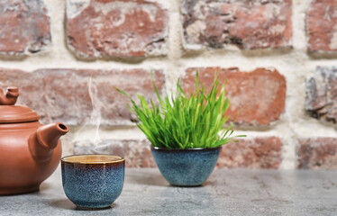 Hot green tea in a blue bowl, selective focus, steam rises above the cup, next to a clay teapot. Gray stone table, brick vintage background. Close-up, tea ceremony, minimalism, place for text