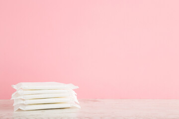 Stack of white sanitary towel packs on wooden table at light pink wall background. Pastel color. Closeup. Female hygiene. Front view. Empty place for text.