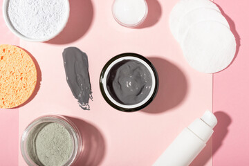 An open cosmetic jar, against the background of a smeared cream or cosmetic face mask. Purifying and moisturizing clay mask. Top view, flat lay