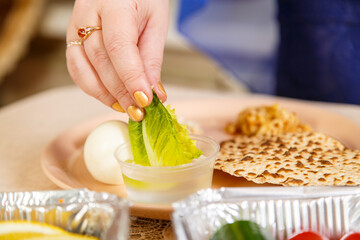 A woman's hand dips a leaf of lettuce in salt water during the Pesach Seder.