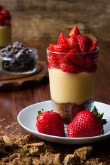 Sweet strawberry trifle dessert in glass with pudding and cookies on wooden background