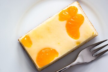 A piece of cheesecake with orange tangerine slices on a white plate with fork