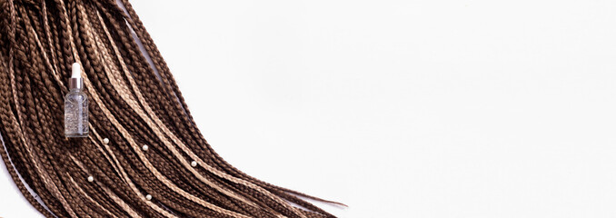 Banner. Thin brown African braids and a jar of care oil on a white background. Hair close-up, braided dreadlocks, afro style - obrazy, fototapety, plakaty