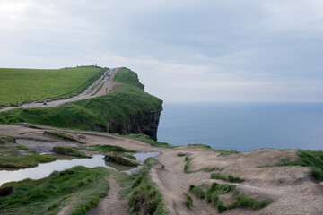 Beautiful cliffs at Moher. Green field, path and ocean. People in the distance taking pictures. Ireland.