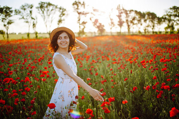 Young woman having fun in the middle of the red poppy field at spring. Girl wearing white light dress enjoys freedom and good weather. Spring and joy concept.