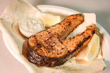 Grilled salmon steak on the plate with lemon slice, sauce and pita. Street food concept. 