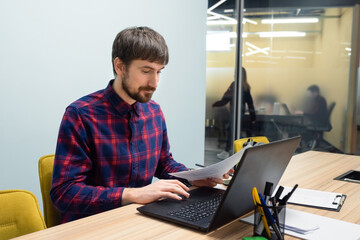 Businessman sitting at an office table working on a laptop. Portrait of a young man sitting at his desk in the office
