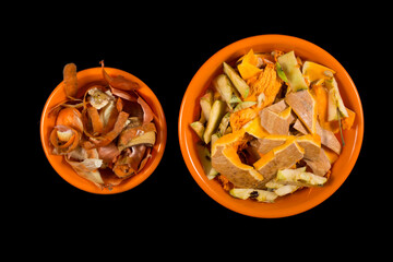 Kitchen waste isolated on black. Peels from vegetables  on bowl. Organic waste in orange bowl.