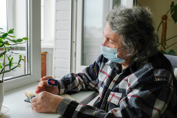An elderly man in a protective mask on self-isolation at home, measures the level of oxygen in the...