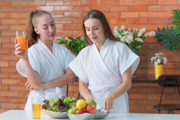 two women in bathrobe cooking a morning food vegetable salad at pantry preparing at home. A...