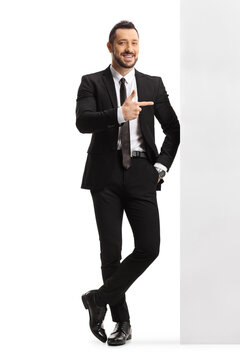 Professional man in a suit and tie leaning on a wall and pointing to the side