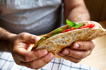 Piadina Romagnola with mozzarella cheese, tomatoes, ham and rocket salad in a man's hands. Italian flatbread or open sandwich. Selective focus.