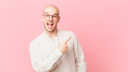 bald man looking excited and surprised pointing to the side and upwards to copy space