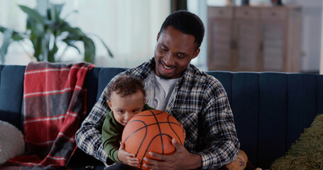 Cheerful african american daddy holding baby boy son upbringing, playing funny games with toys spending weekend at home.