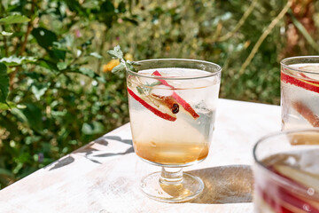 Fresh and healthy cocktail or mocktail with apple, ice, cinnamon and herbs. Refreshing summer drink on nature background