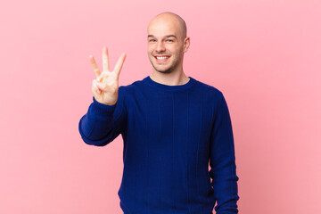 bald man smiling and looking friendly, showing number three or third with hand forward, counting...