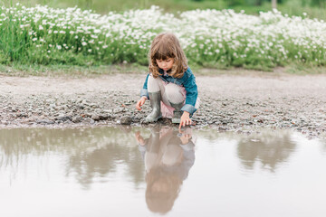 Portrait of little cute girl on the field with daisies and water.