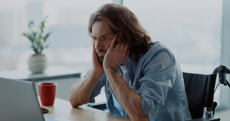 Young depressed office worker sitting by desk worry about work. Disabled invalid young man...