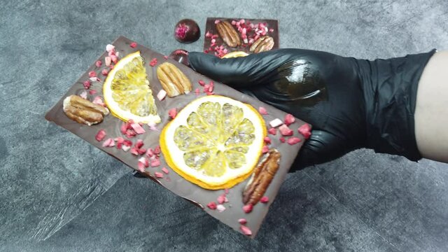 Handmade chocolate bar is shown holding in your hands. Close-up luxury handmade chocolate with spices, dry berries and nuts.