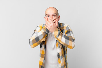 bald man covering mouth with hands with a shocked, surprised expression, keeping a secret or saying...
